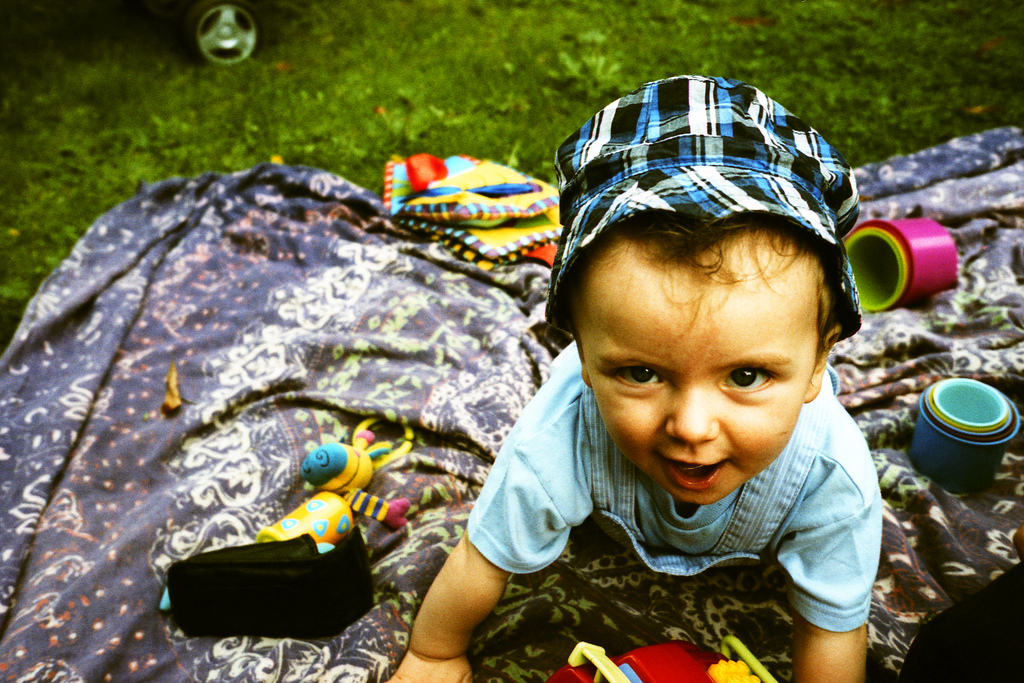 A film photo in high colour of a baby on a rug with a cheeky face
