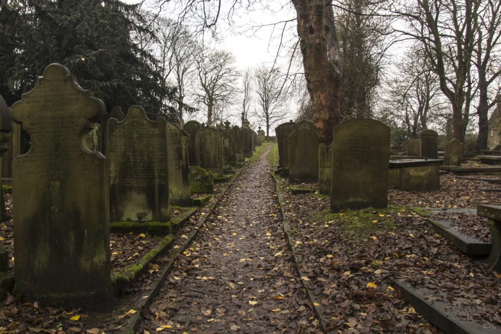 A path through a graveyard, on a dull day with autumn leaves on the ground