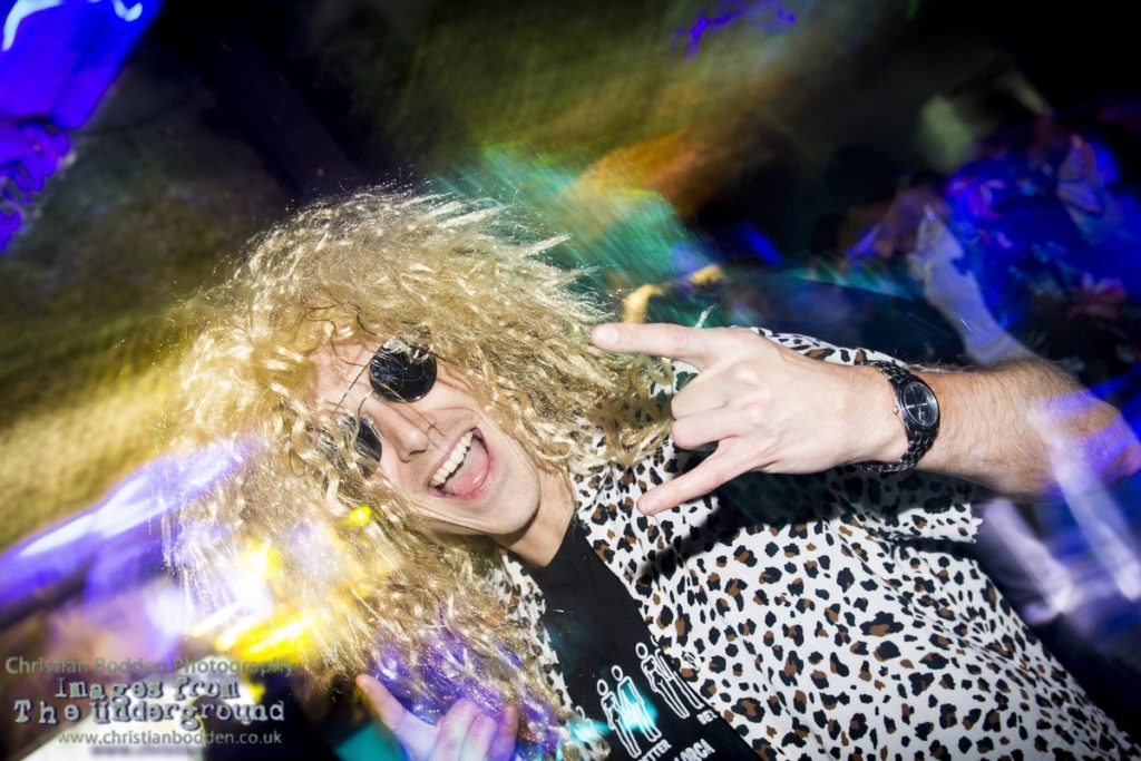 A man in a nightclub wearing a blonde wig and sunglasses